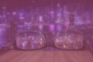 Online sichtbar werden symbolisiert durch eine Brille, durch welche der Blick auf eine nächtliche Skyline klar ist, während der Rest verschwommen ist.