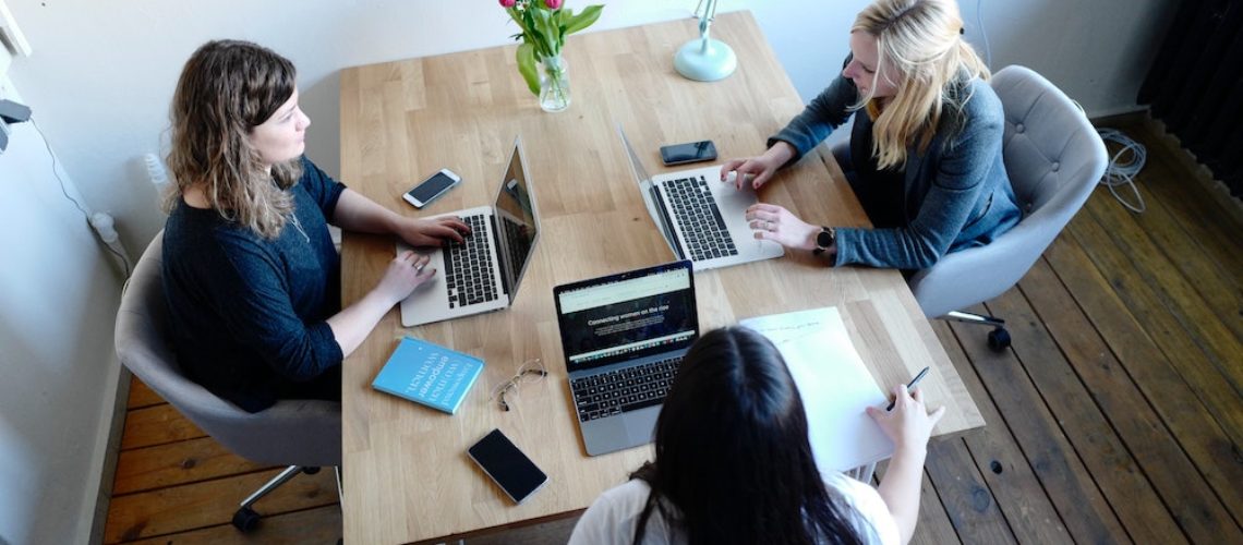 Vogelperspektive auf drei Frauen an einem Tisch, die vor ihren Laptops sitzen. Die eine Frau könnte den anderen Beiden Frauen wertvolle SEO-Tipps für Anfänger und Anfängerinnen geben